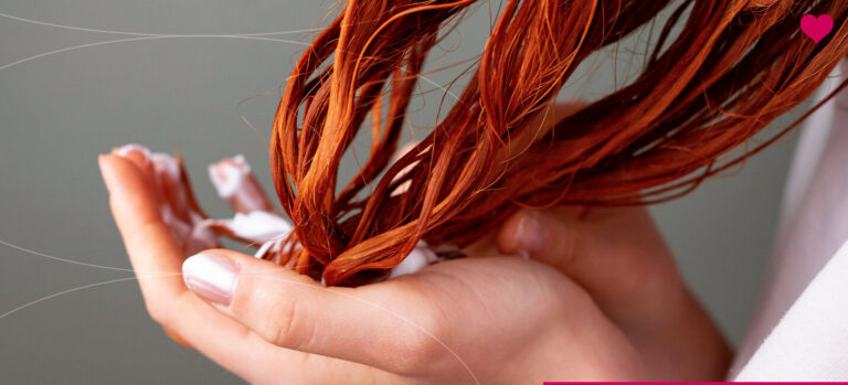 Mãos segurando cabelos ruivos e pétalas de flores.