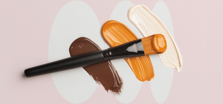 Pincel e tintas em tons de pele sobre fundo rosa