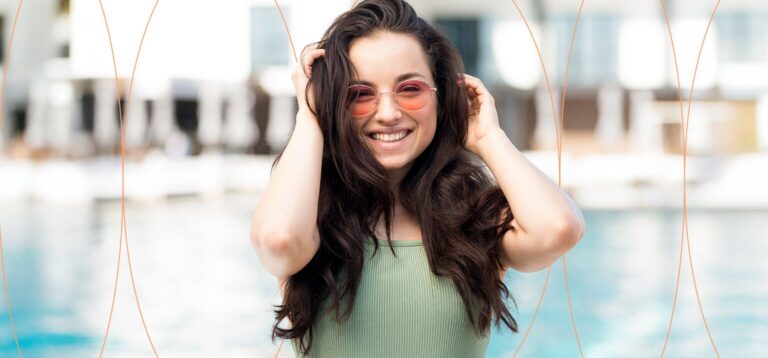 Mulher sorrindo com óculos de sol à beira da piscina