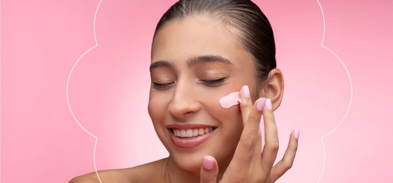 Mulher aplicando creme facial em fundo rosa