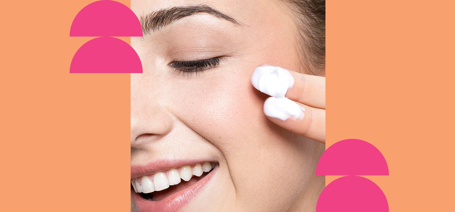 Mulher aplicando creme no rosto com sorriso