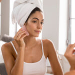 Mulher na frente de um espelho, com uma toalha na cabeça, fazendo skincare para pele oleosa.