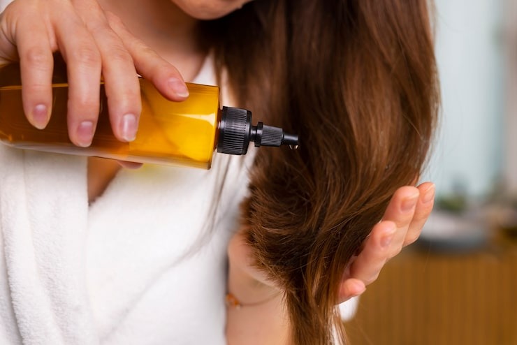 Mulher de cabelo liso passando óleo de rícino apenas nas pontas.